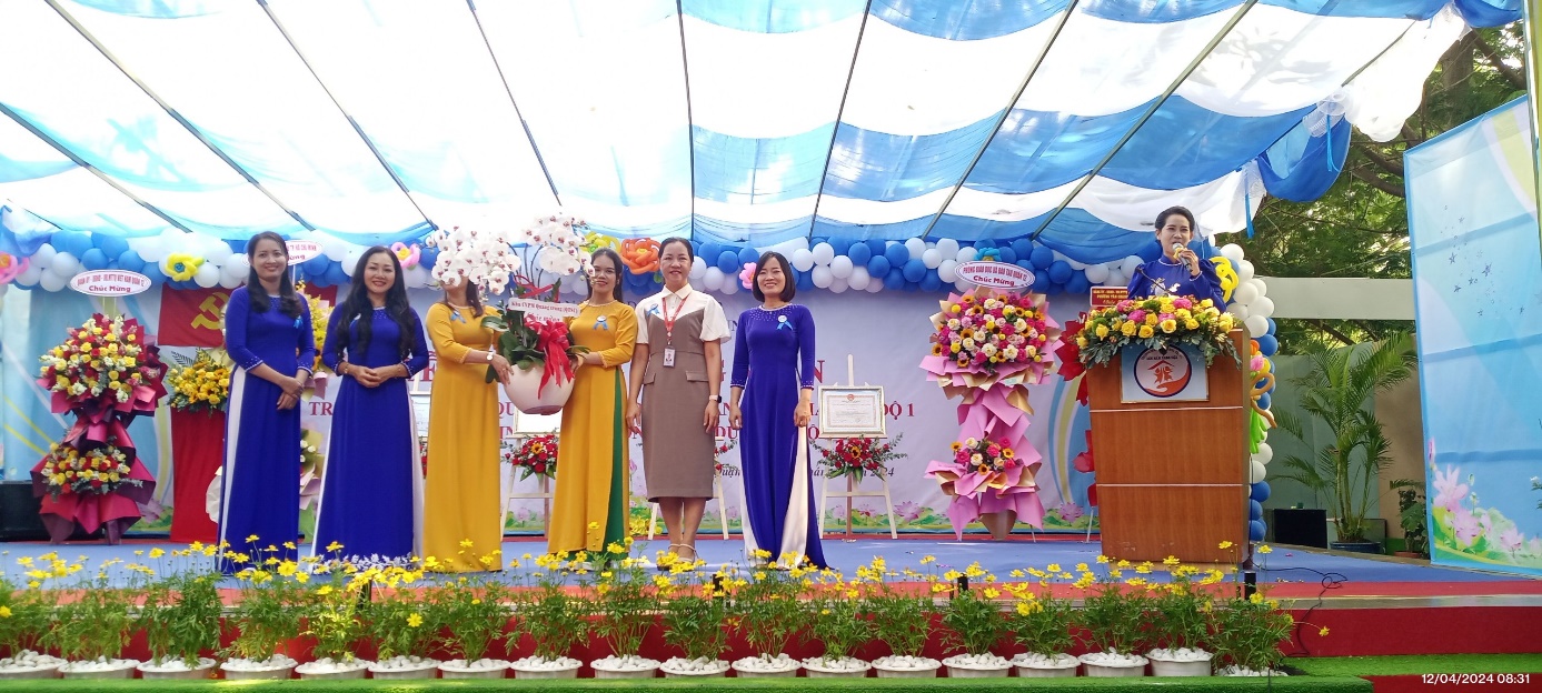 Bà Phạm Thị Kim Phượng – Phó Giám đốc QTSC (thứ 2 từ phải qua) trao lẵng hoa chúc mừng Nhà trường